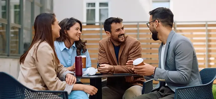 Quatre collègues souriants discutant et partageant un moment convivial autour d’une table en extérieur