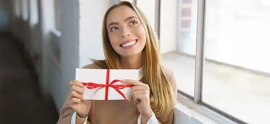 Femme heureuse tenant un cadeau en forme d’enveloppe, entouré d’un ruban rouge